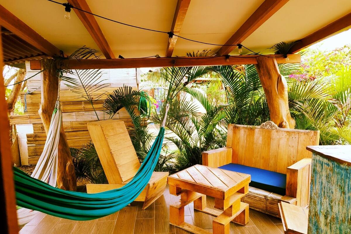 Terraza de madera con una hamaca, mobiliario de madera y vistas a plantas tropicales.