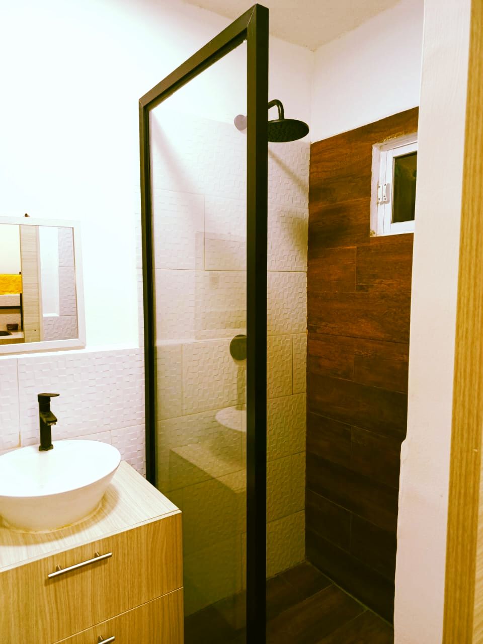Ein modernes Badezimmer mit Duschkabine aus Glas, einem Holzwaschtisch und einem weißen Waschbecken.