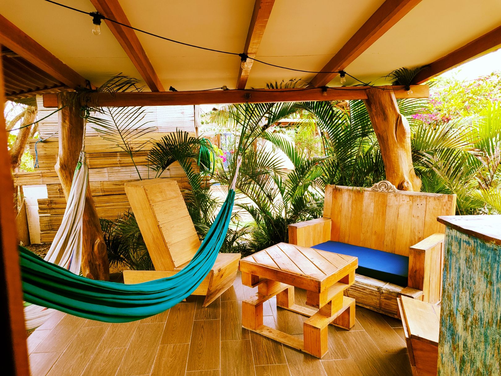 Terraza de madera con una hamaca, mobiliario de madera y vistas a plantas tropicales.
