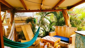 A wooden deck with a hammock, wooden furniture, and a view of tropical plants. - Café Madame (Puerto Lopez)