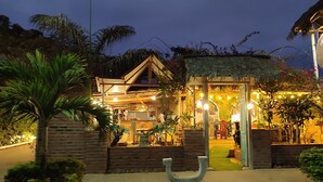 A rustic building with a thatched roof, surrounded by lush greenery and palm trees. - Café Madame (Puerto Lopez)