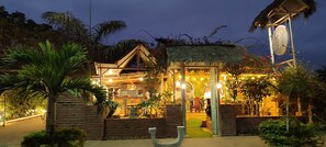 A rustic building with a thatched roof, surrounded by lush greenery and palm trees. - Café Madame (Puerto Lopez)