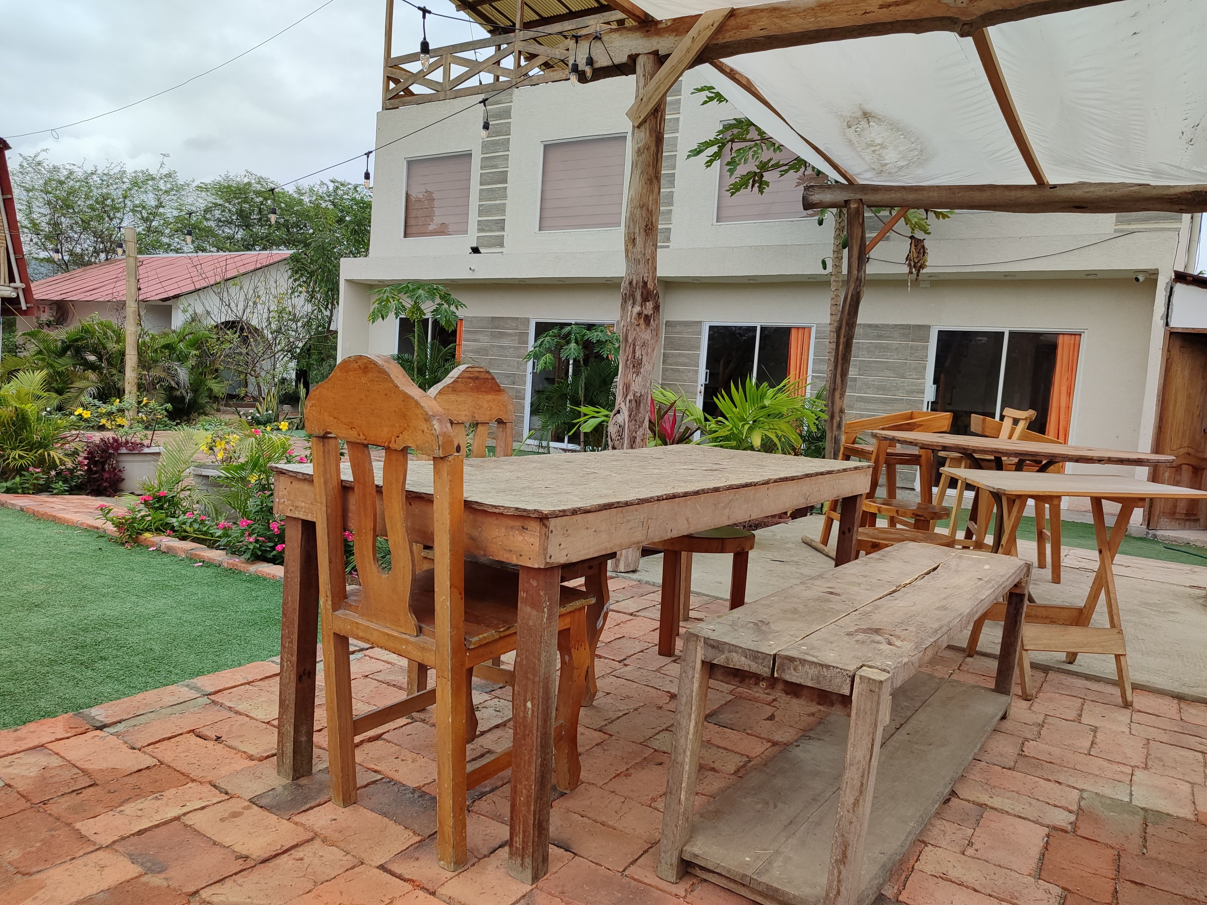 Un patio al aire libre con mobiliario de madera, un pérgola y un jardín con diversas plantas.