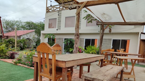 An outdoor patio with wooden furniture, a pergola, and a garden with various plants. - Café Madame (Puerto Lopez)