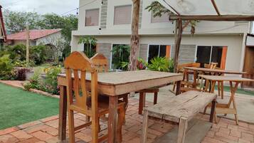 Un patio al aire libre con mobiliario de madera, un pérgola y un jardín con diversas plantas.