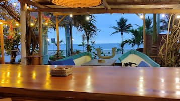 A beachside restaurant with a wooden bar, outdoor seating, and a view of the ocean.