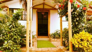 A pathway leading to a building entrance with a green mat, surrounded by lush greenery and bamboo poles. - Café Madame (Puerto Lopez)