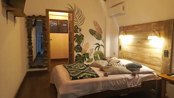 Un dormitorio con cabecera de madera, cama con muchas almohadas, aire acondicionado de pared y puerta que da a otra habitación.