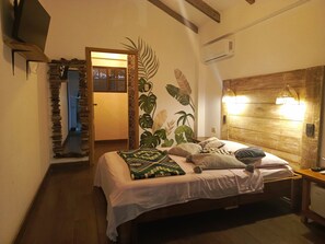 A bedroom with a wooden headboard, a bed with multiple pillows, a wall-mounted air conditioner, and a door leading to another room. - Café Madame (Puerto Lopez)