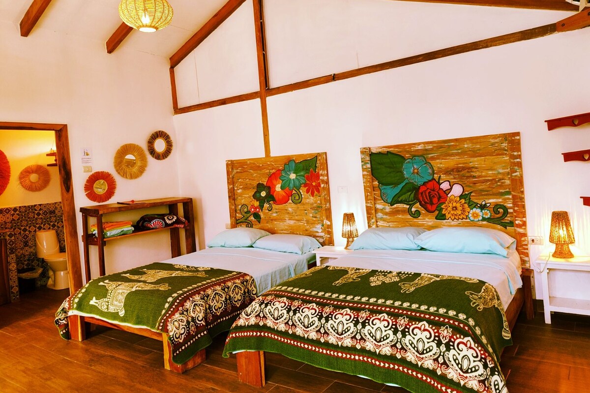 A room with two beds, wooden beams, a hanging light fixture, and floral artwork on the walls.