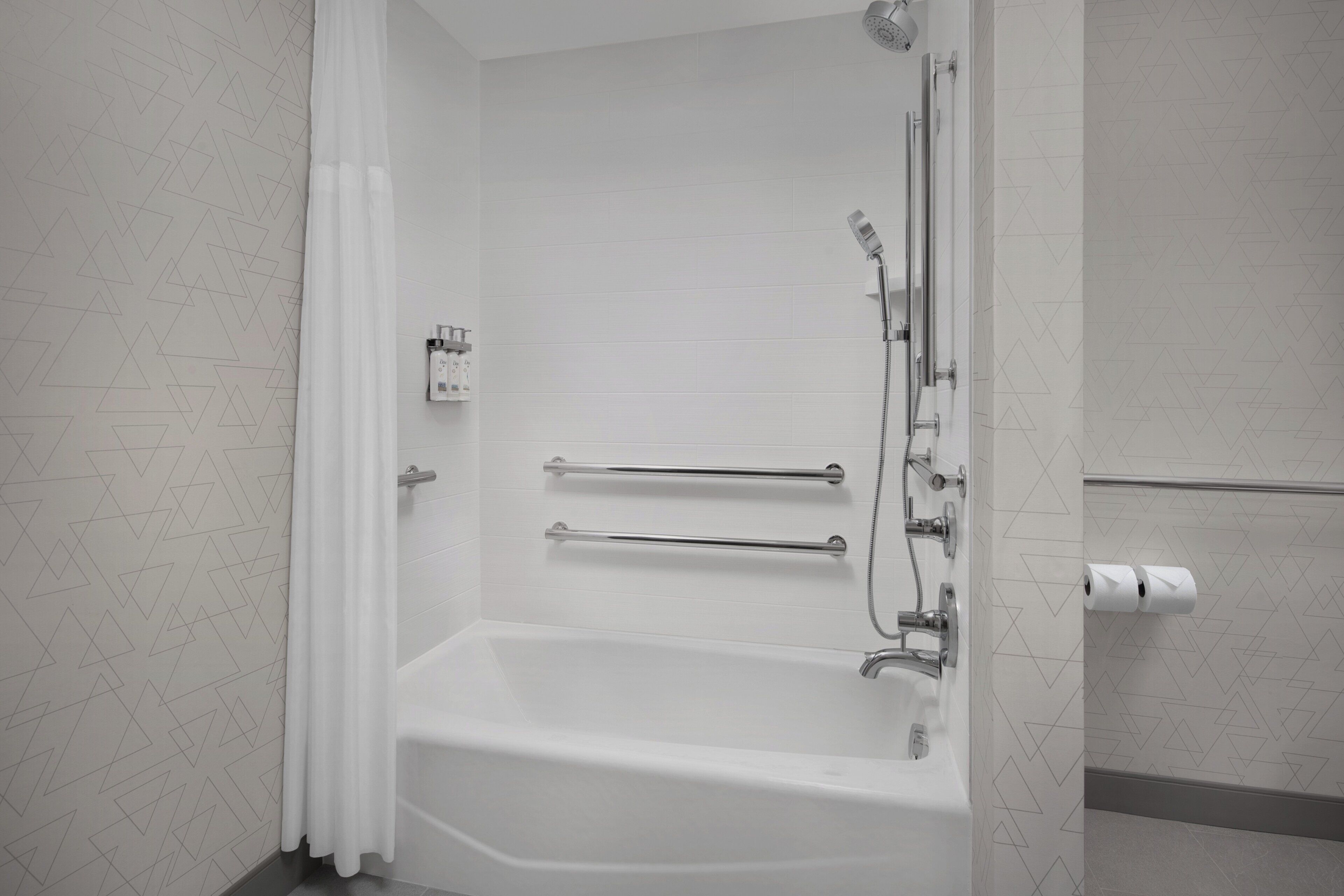 Un bagno moderno con una vasca da bagno bianca, maniglie di sostegno e un soffione.