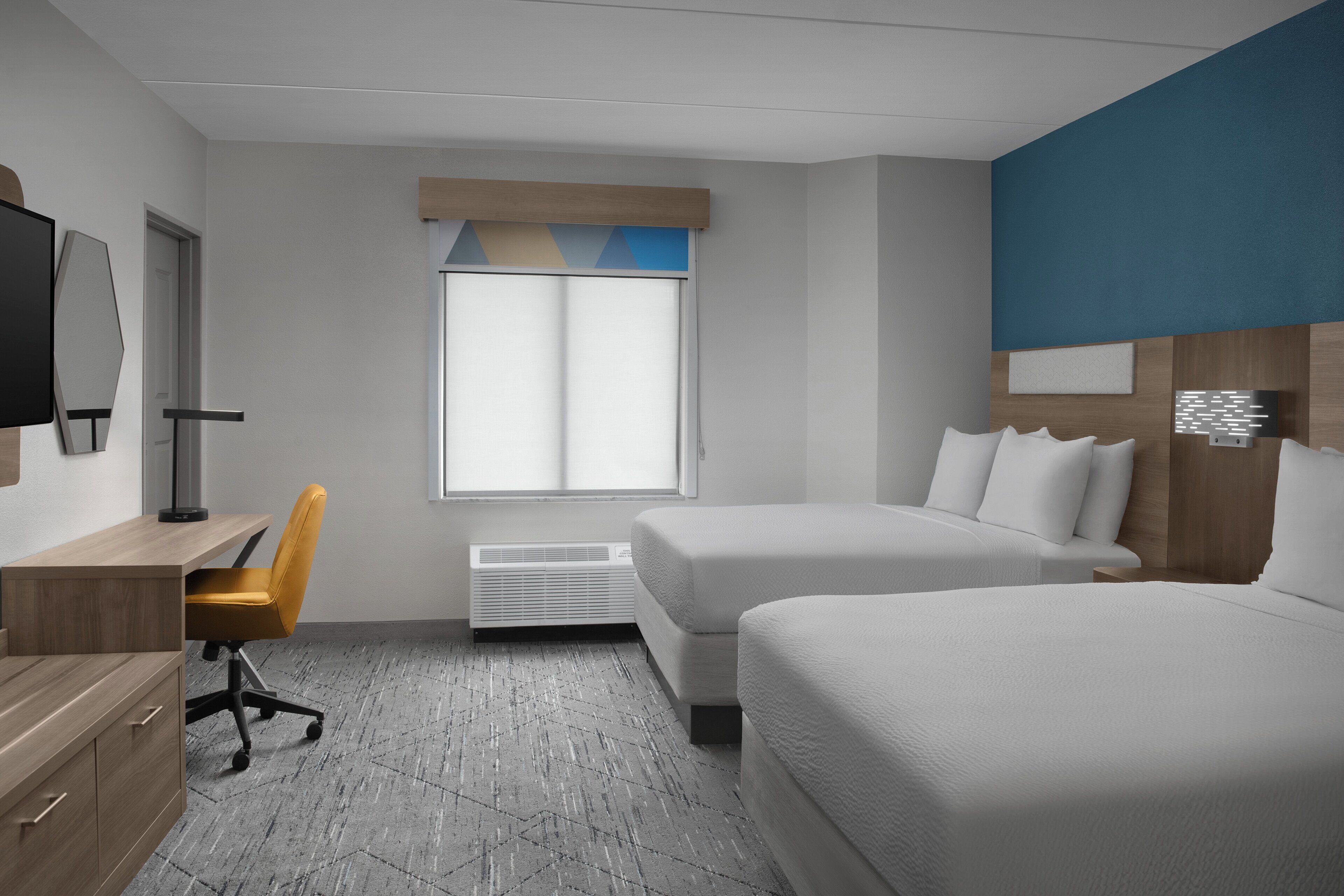 A hotel room with two beds, a desk with a chair, a TV, and a window with blinds.