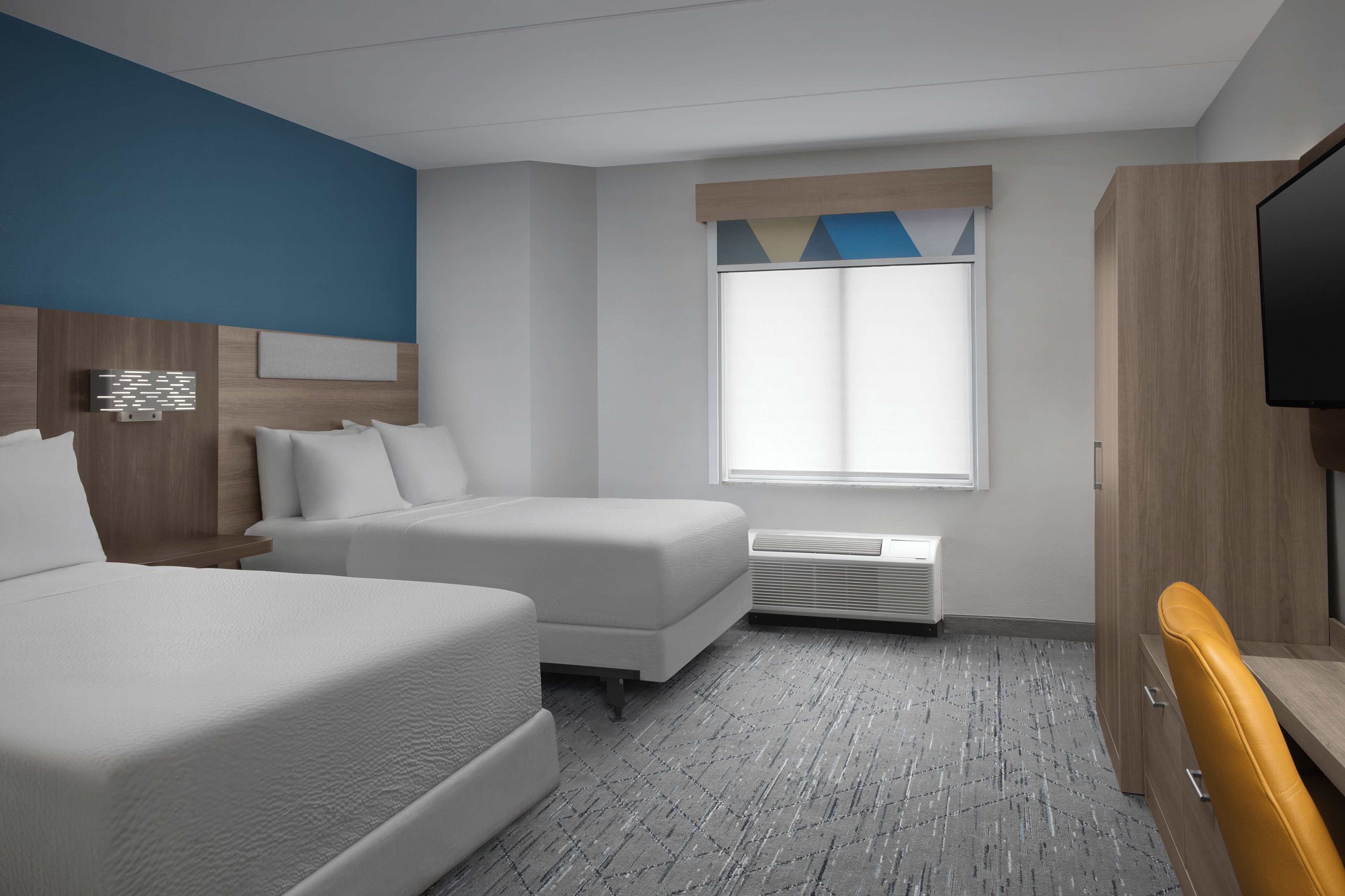 Quarto de hotel com duas camas, televisão, escrivaninha e janela com persianas.