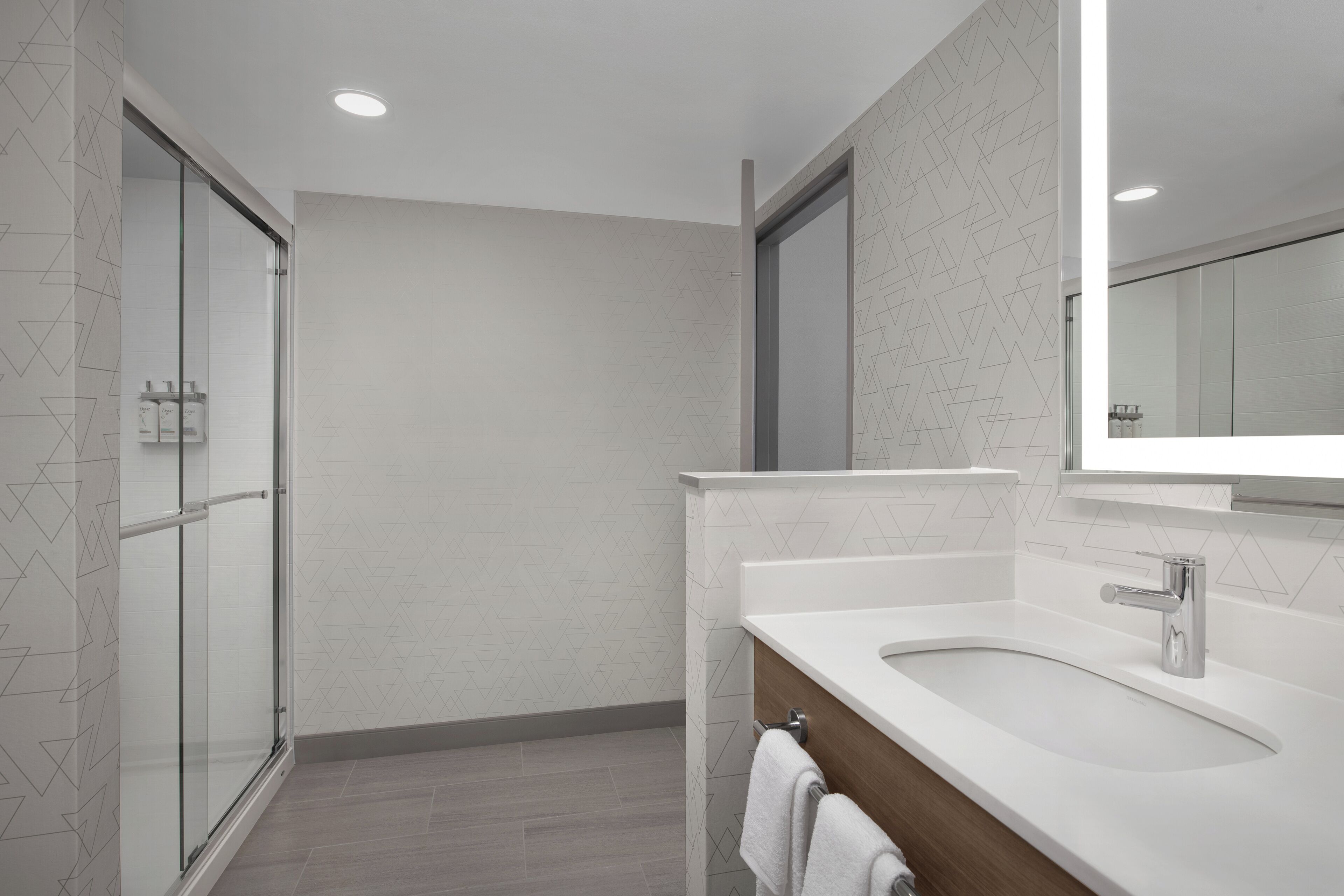 Un baño moderno con cabina de ducha de vidrio, un lavabo blanco con mueble de madera y un espejo grande.