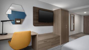 A modern hotel room with a wooden desk, a yellow chair, a flat-screen TV, a wardrobe, and a bed.