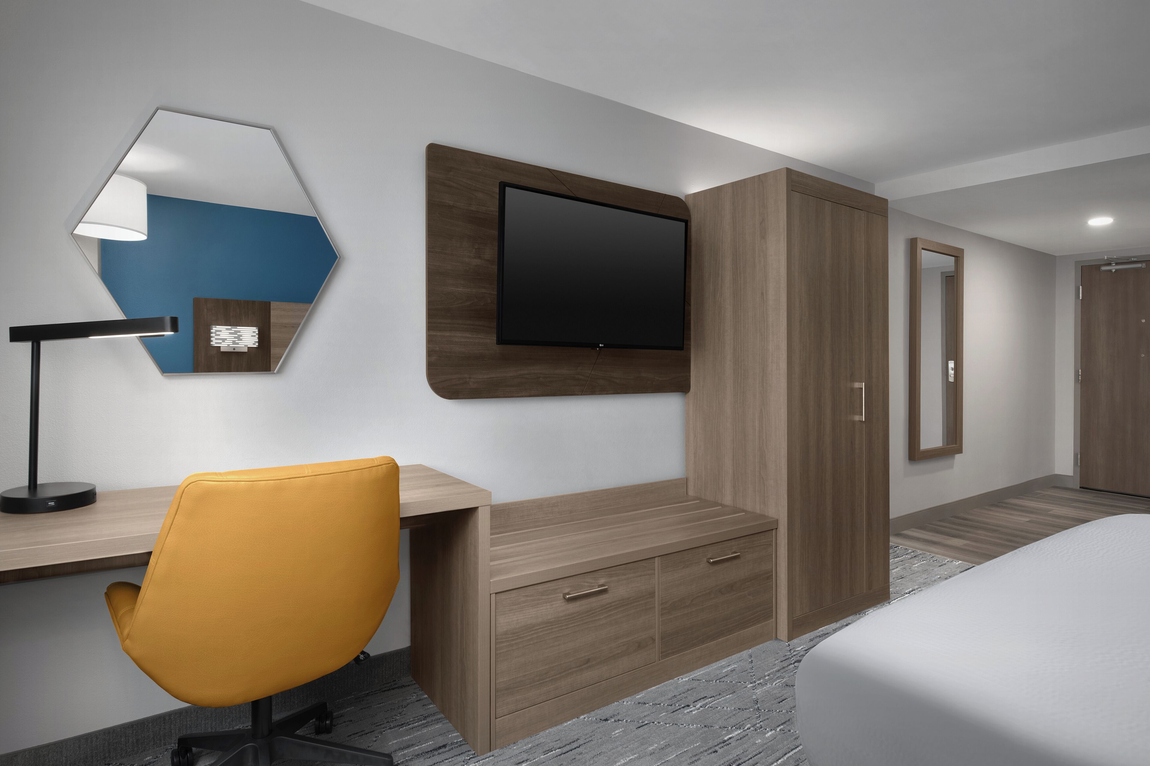Een moderne hotelkamer met een houten bureau, een gele stoel, een flatscreen televisie en een kledingkast.