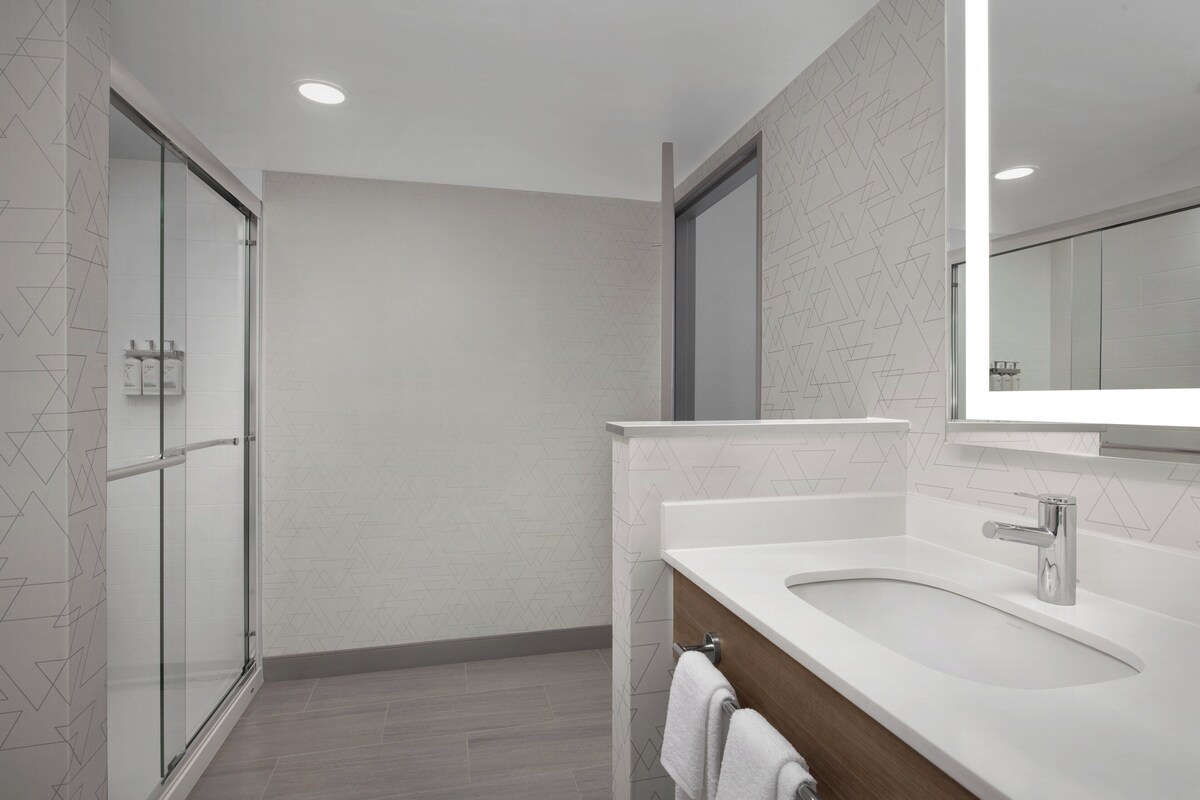 A modern bathroom with a glass shower enclosure, a white sink with a wooden vanity, and a large mirror above the sink.