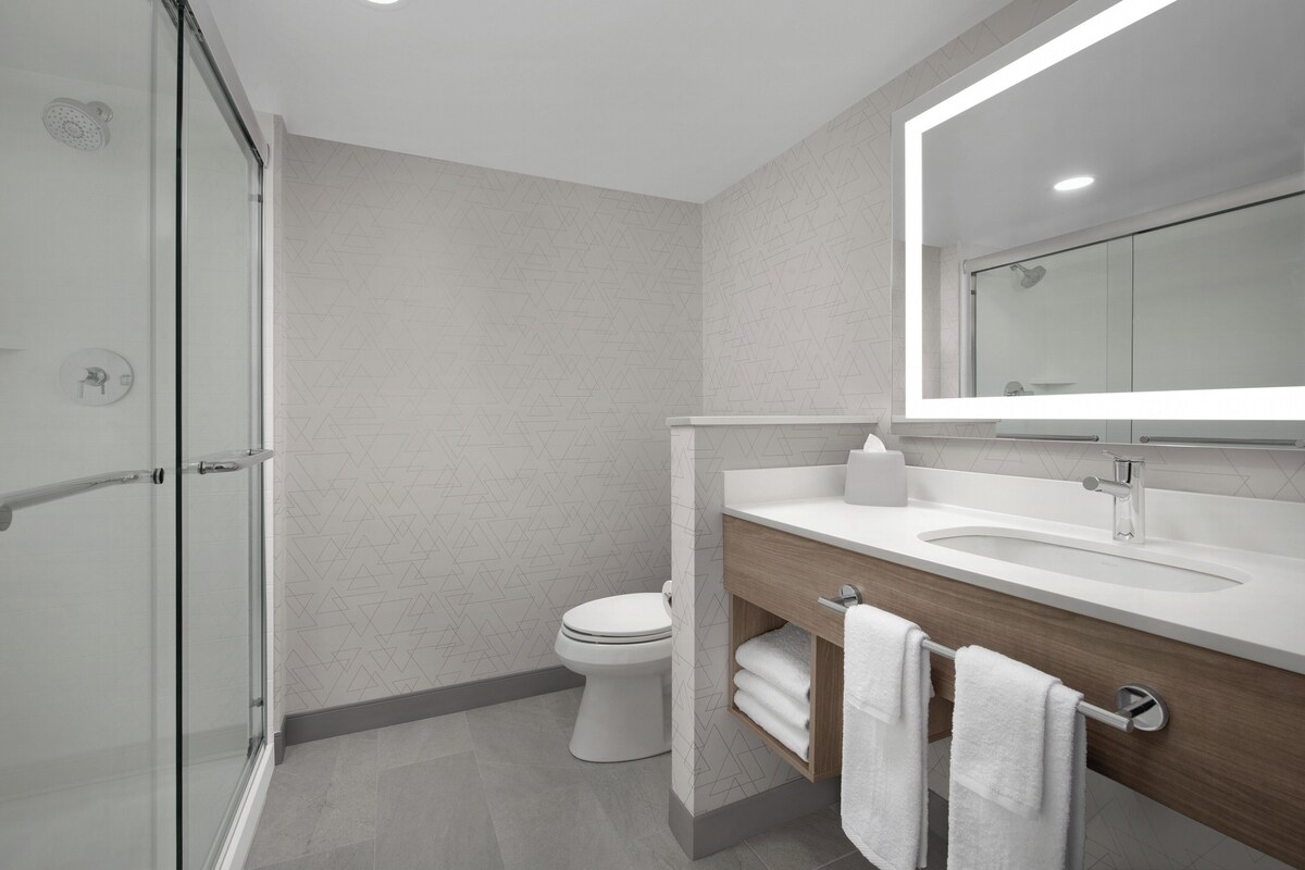 A modern bathroom with a glass shower enclosure, a white toilet, and a wooden vanity with a mirror above the sink.