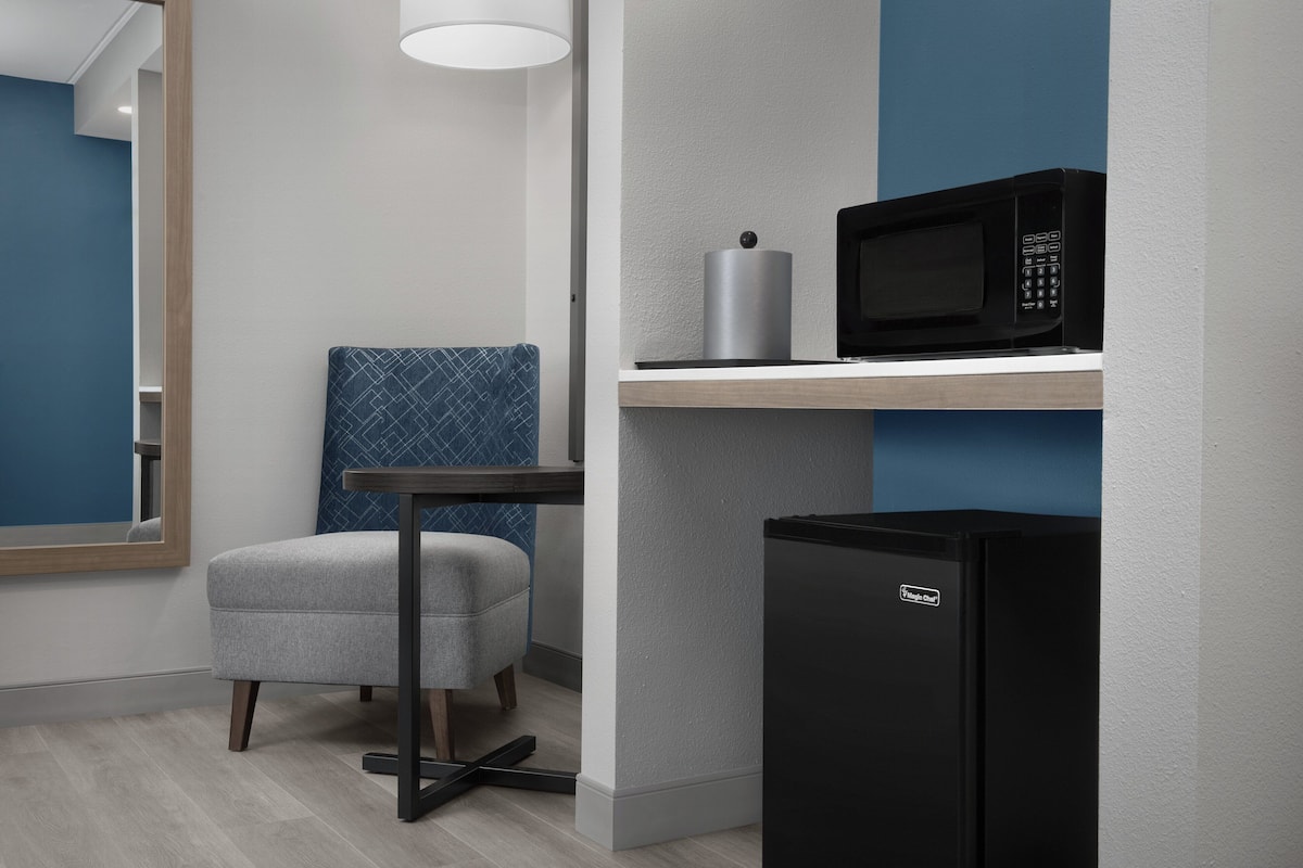 A compact kitchenette with a microwave, a refrigerator, a chair, and a table.