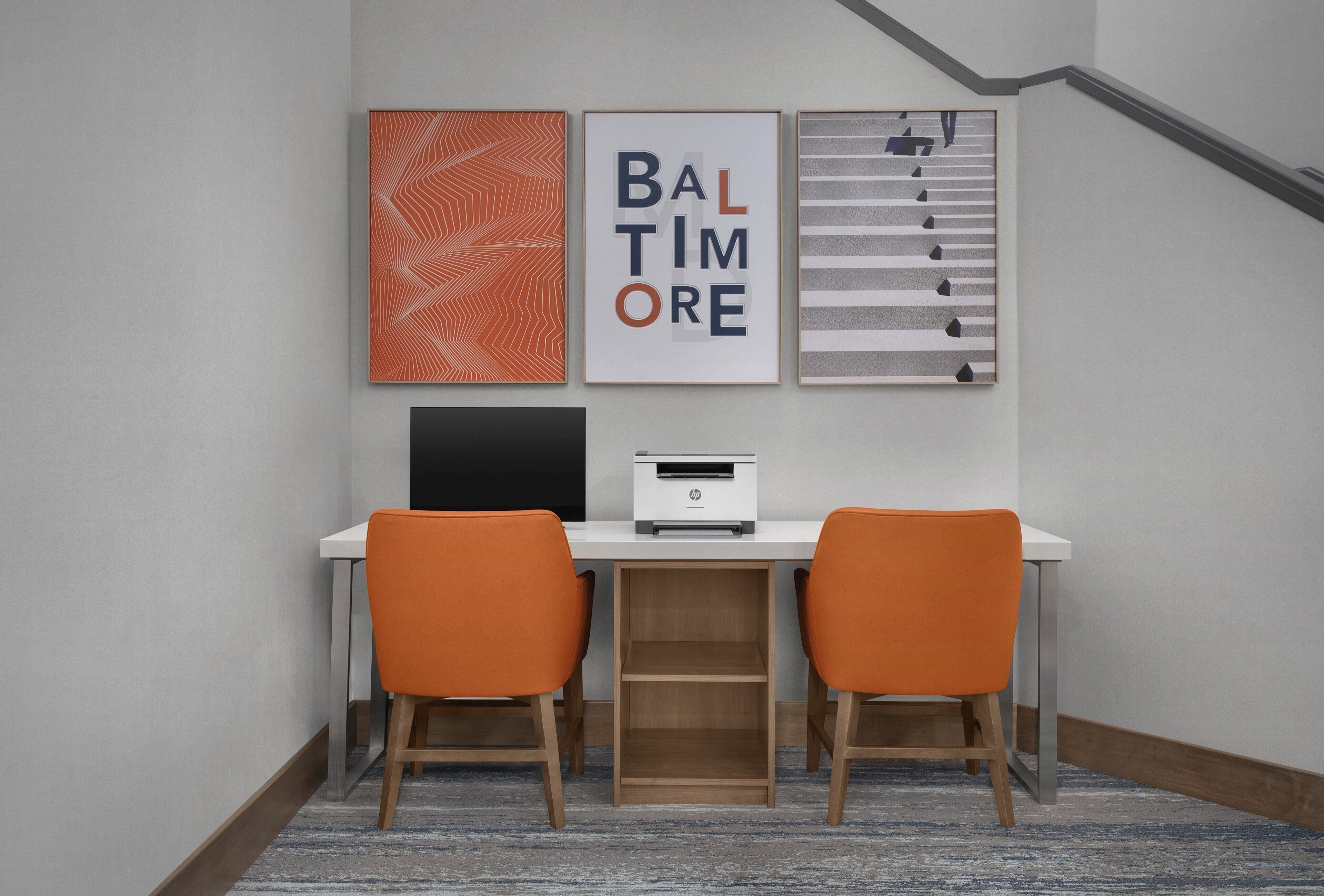 A room with a desk, two chairs, a printer, and three framed artworks on the wall.