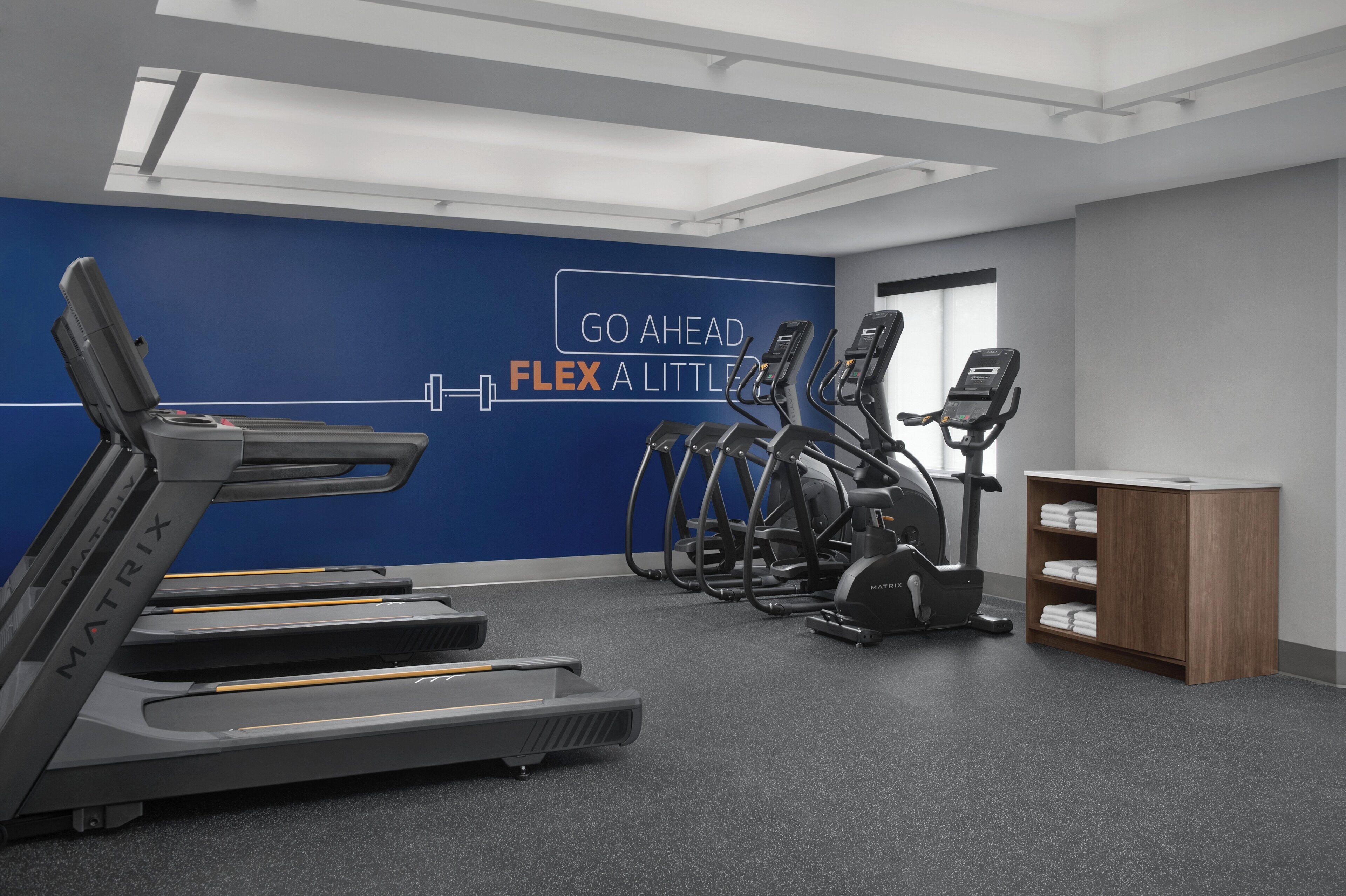 Une salle de sport équipée de tapis de course, de vélos elliptiques et d’un mur orné de citations motivantes.