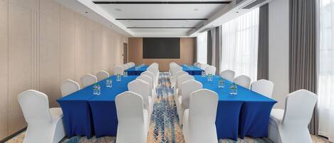 Un salón de conferencias con una mesa larga, sillas blancas y manteles azules.