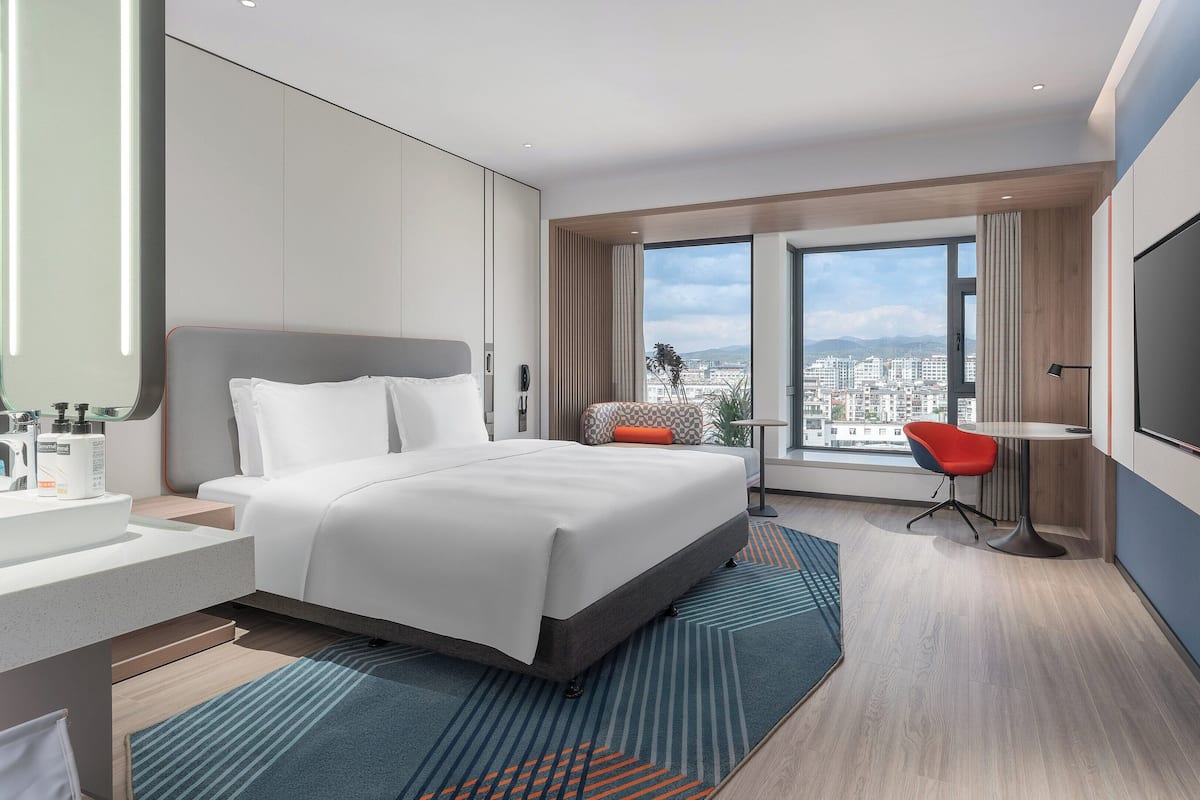 Une chambre d’hôtel moderne dotée d’un grand lit, d’un bureau, d’une chaise, d’une télévision et offrant une vue sur la ville.