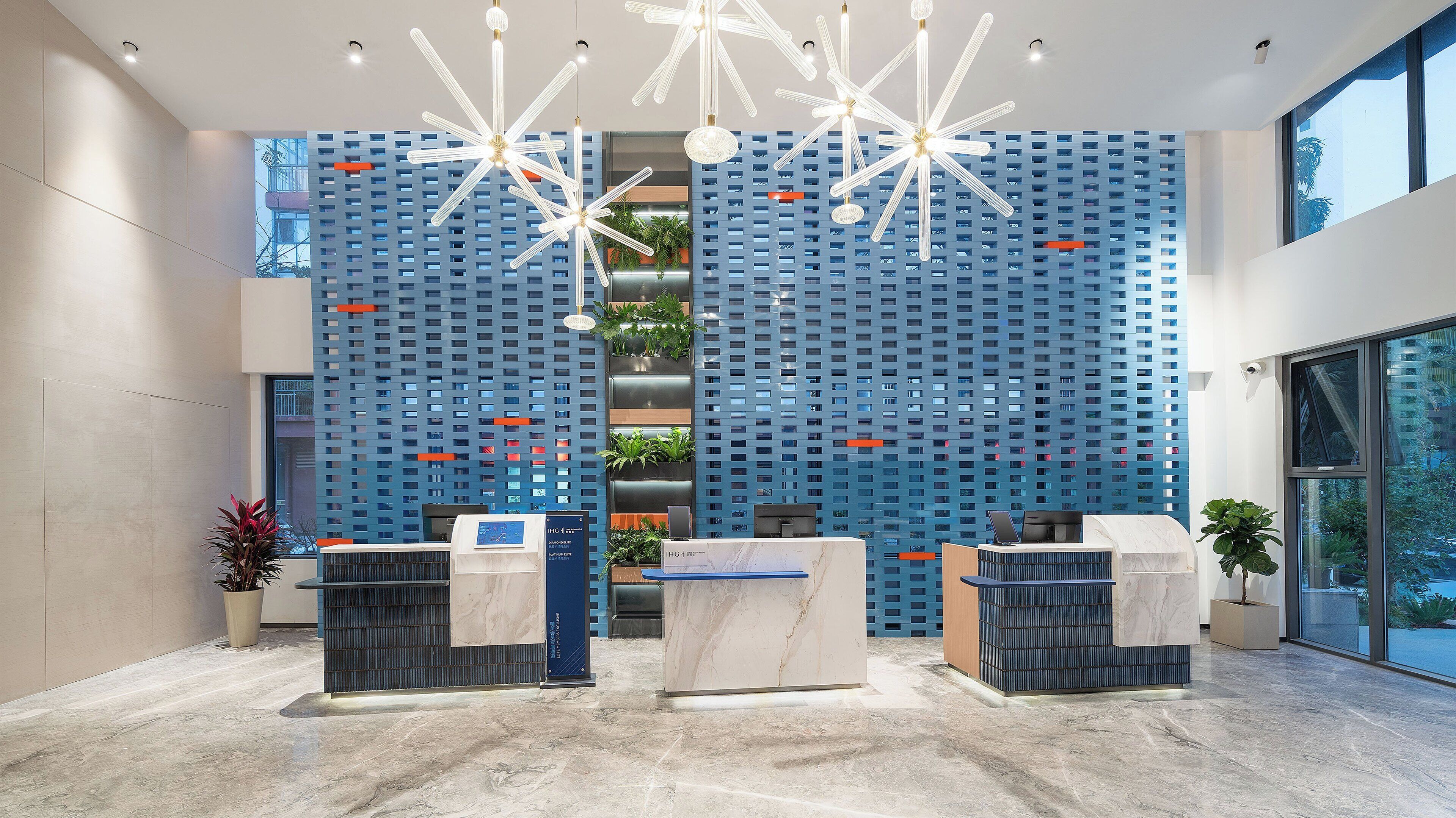 A modern reception area with a blue patterned wall, marble reception desks, and hanging light fixtures.