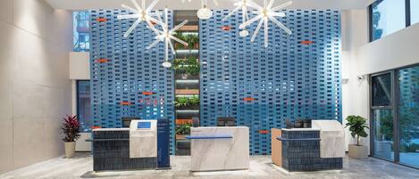 A modern reception area with a blue patterned wall, marble reception desks, and hanging light fixtures.