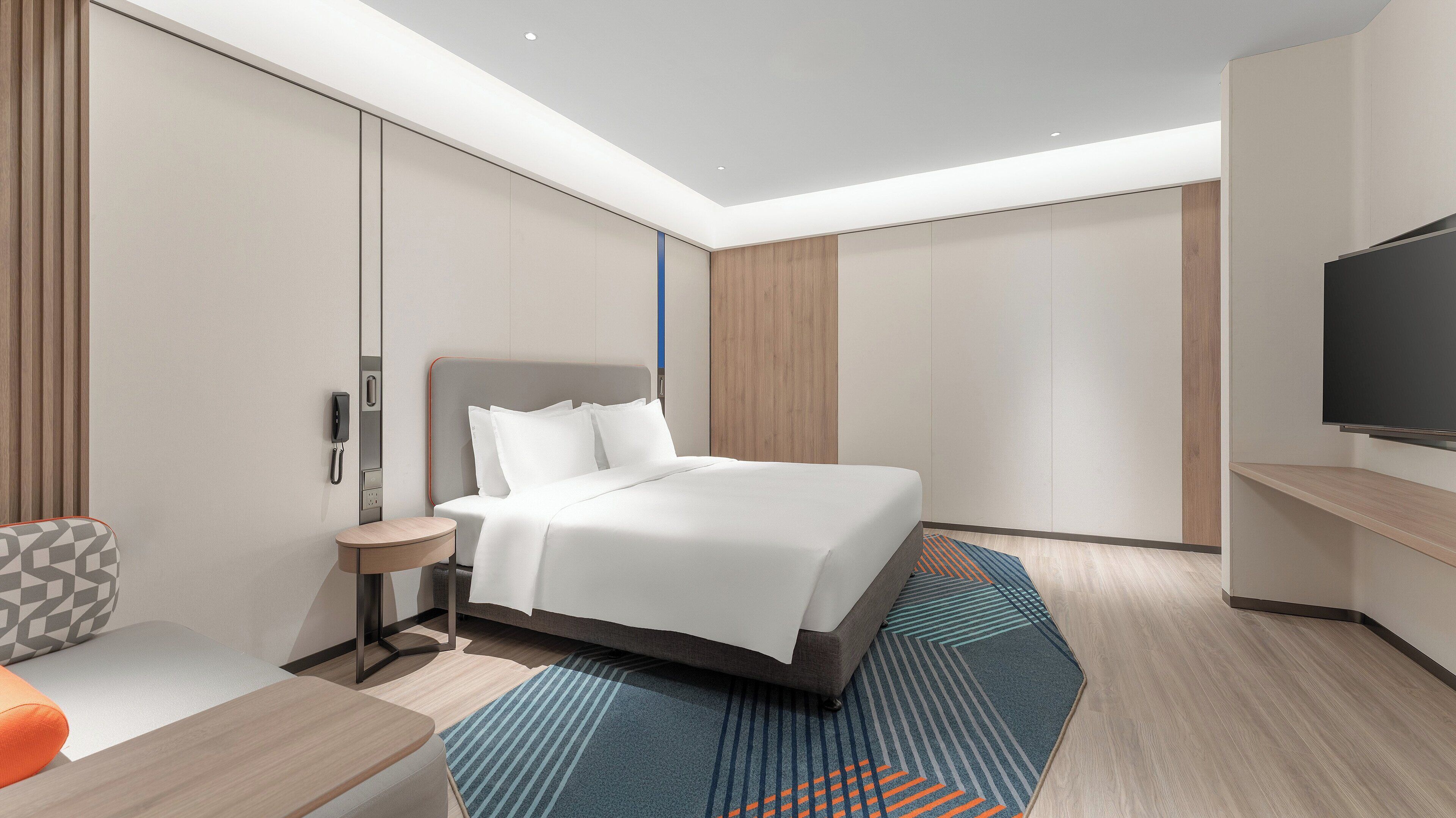Een moderne hotelkamer met een groot bed, een flatscreen televisie, een nachtkastje en een zithoek met een gestreept fauteuil.