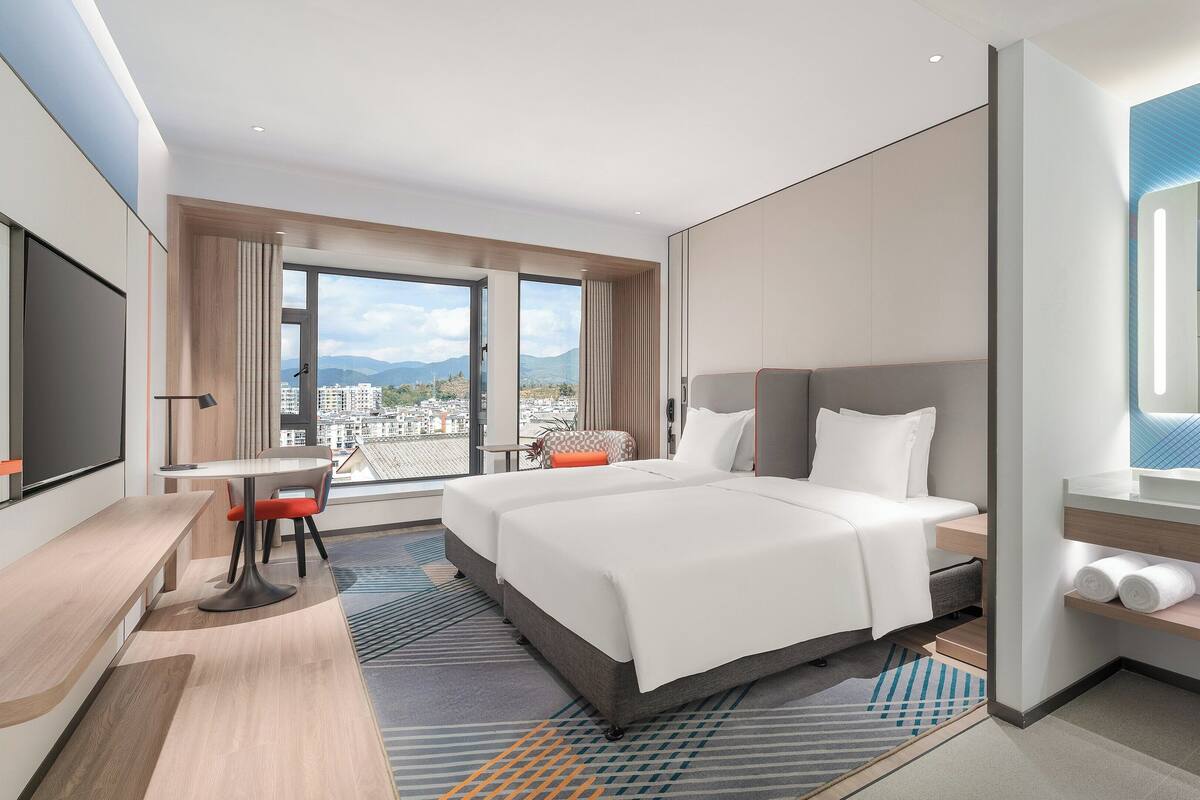 Une chambre d’hôtel avec un grand lit, un bureau, une chaise, une télévision et une salle de bain avec un miroir, le tout offrant une vue sur la ville.