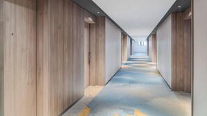 Moderni hotellikäytävä, jossa on puuseinät, kuvioitu matto ja suora katto, johon on upotettu valaisimet.