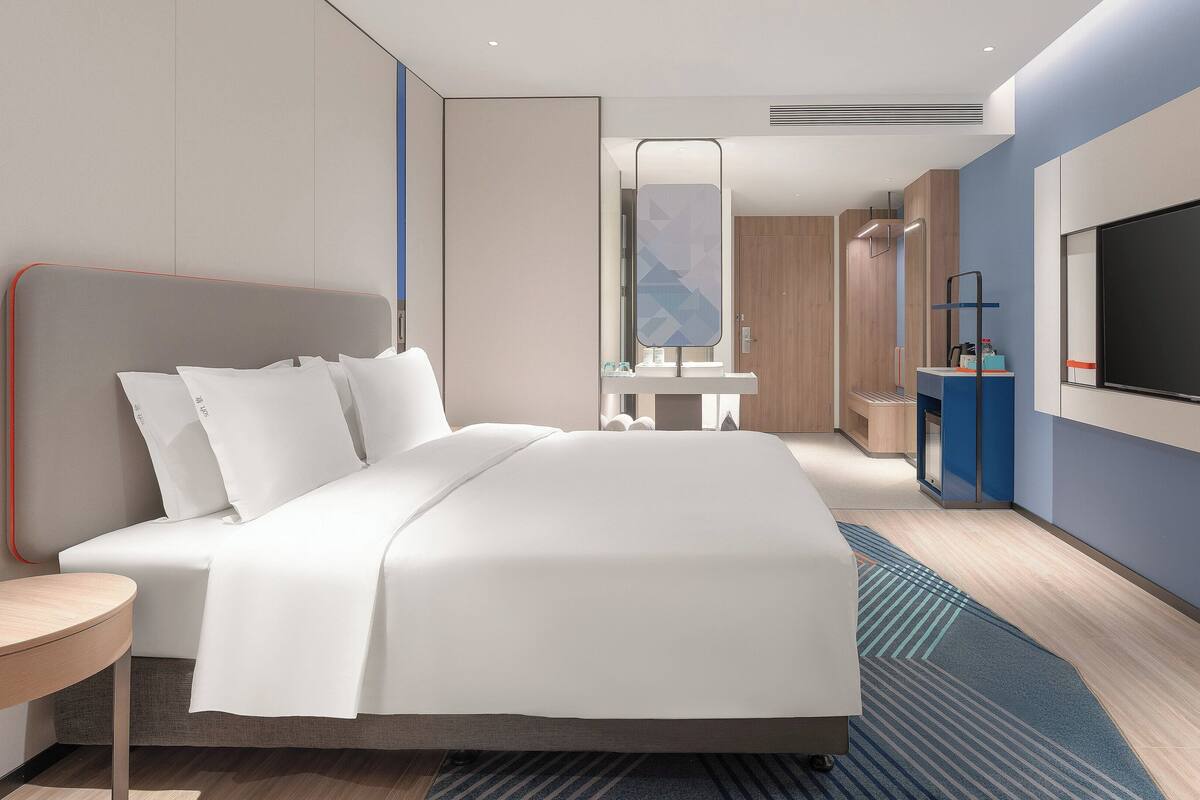 Une chambre d’hôtel moderne avec un grand lit, une télévision, un petit bureau et une salle de bain visible au fond.