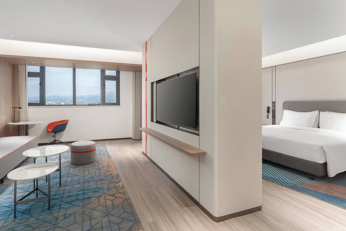 Une chambre d’hôtel moderne équipée d’un canapé, d’une petite table, d’une télévision, d’un lit et d’une fenêtre donnant sur la ville.