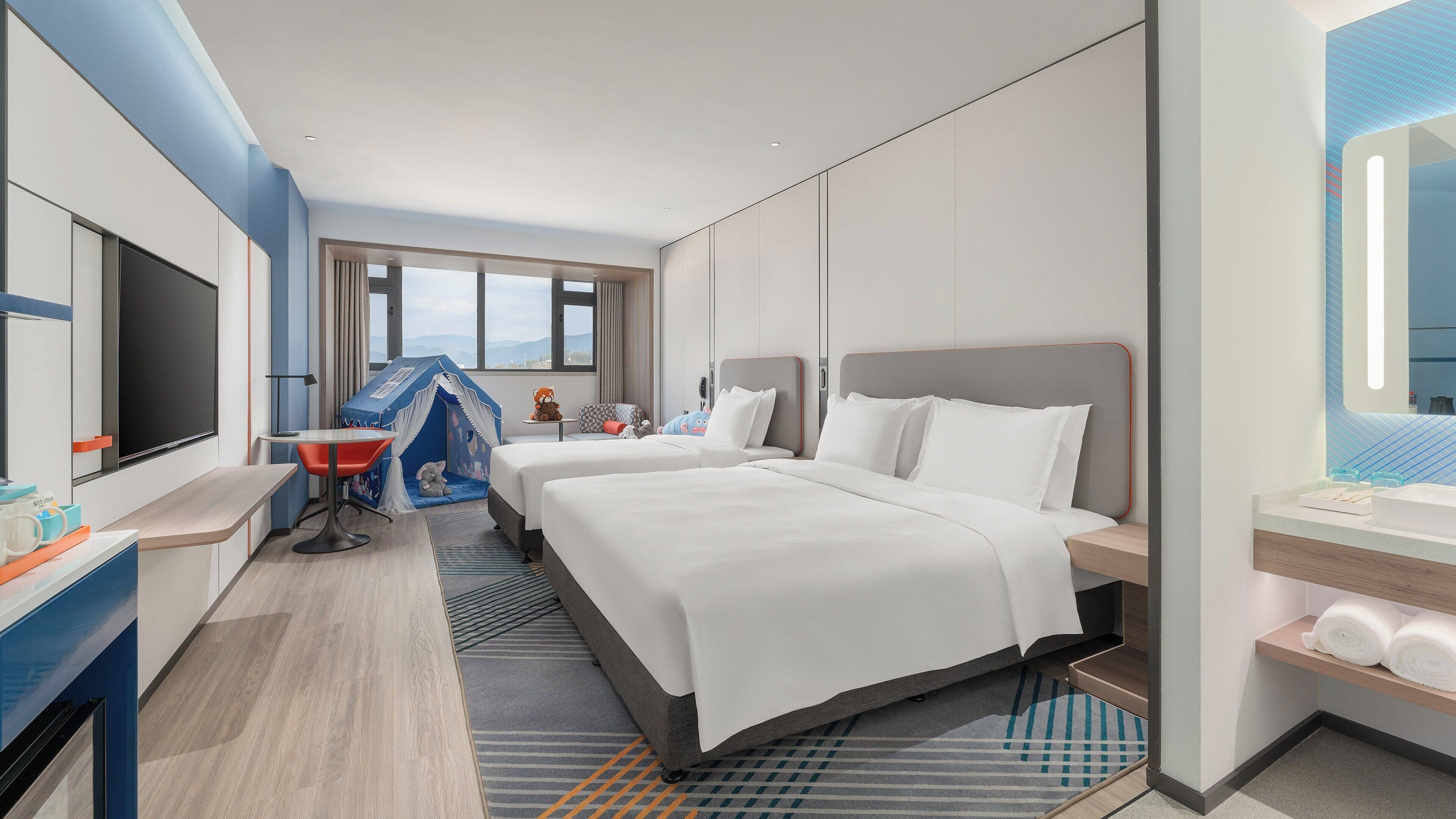 Habitación de hotel con una cama grande, un escritorio, una silla, un televisor y una zona de juegos para niños.