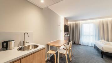 A modern hotel room with a kitchenette, a bed, and a seating area.
