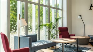 Ein modernes Zimmer mit großen Fenstern, einem roten Sessel, einem blauen Sofa und einem kleinen Tisch.