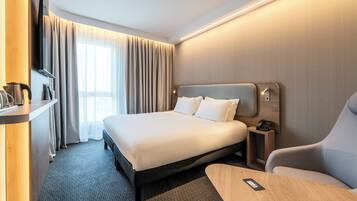 Habitación de hotel con una cama grande, un escritorio con teléfono, una silla, un televisor y una ventana con cortinas.