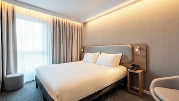 A hotel room with a large bed, a bedside table with a phone, a chair, and a window with curtains.
