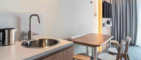 A modern hotel room with a kitchenette, a sink, a wooden table, and a TV mounted on the wall.