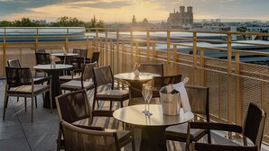 A terrace with tables and chairs, a champagne bucket, and a view of a city skyline with a prominent cathedral. - Holiday Inn Express and Suites Reims Rives De Vesle by IHG (Reims)