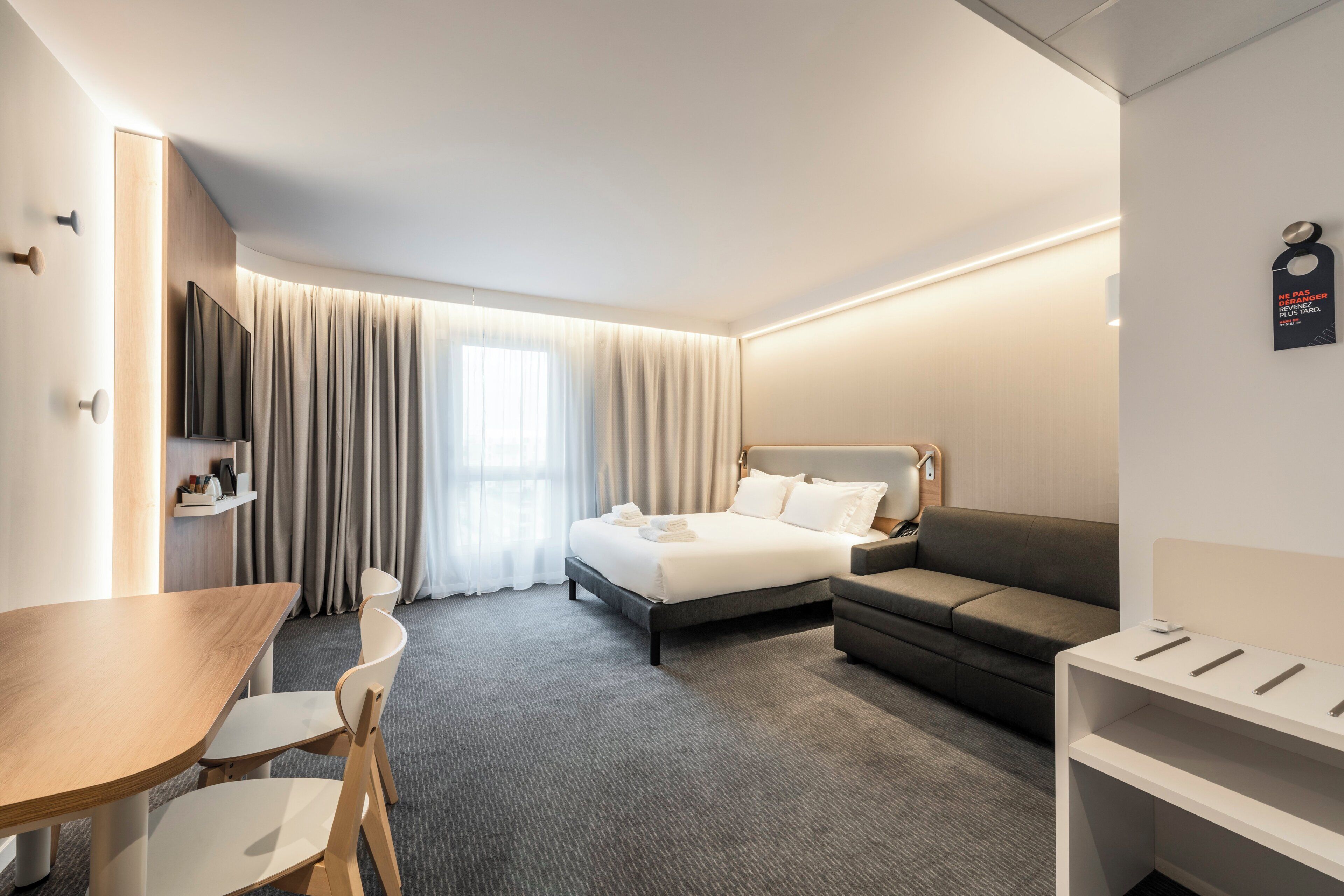 A hotel room with a bed, a sofa, a TV, a desk, and a chair.