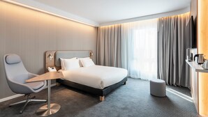 Ein modernes Hotelzimmer mit einem großen Bett, einem Schreibtisch, einem Sessel und einem kleinen Hocker.