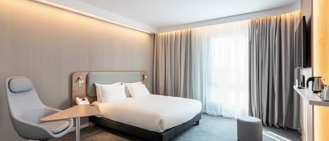 Een moderne hotelkamer met een groot bed, een bureau, een stoel en een klein pouf.