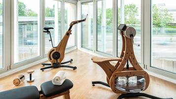A spacious room with large windows, two exercise bikes, a bench, and a pair of dumbbells.