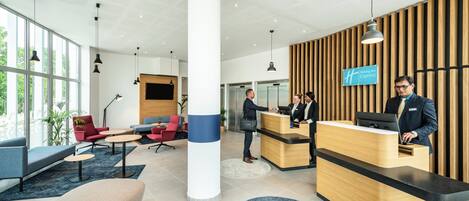 A modern hotel reception area with a wooden reception desk, a large pillar, and seating arrangements.
