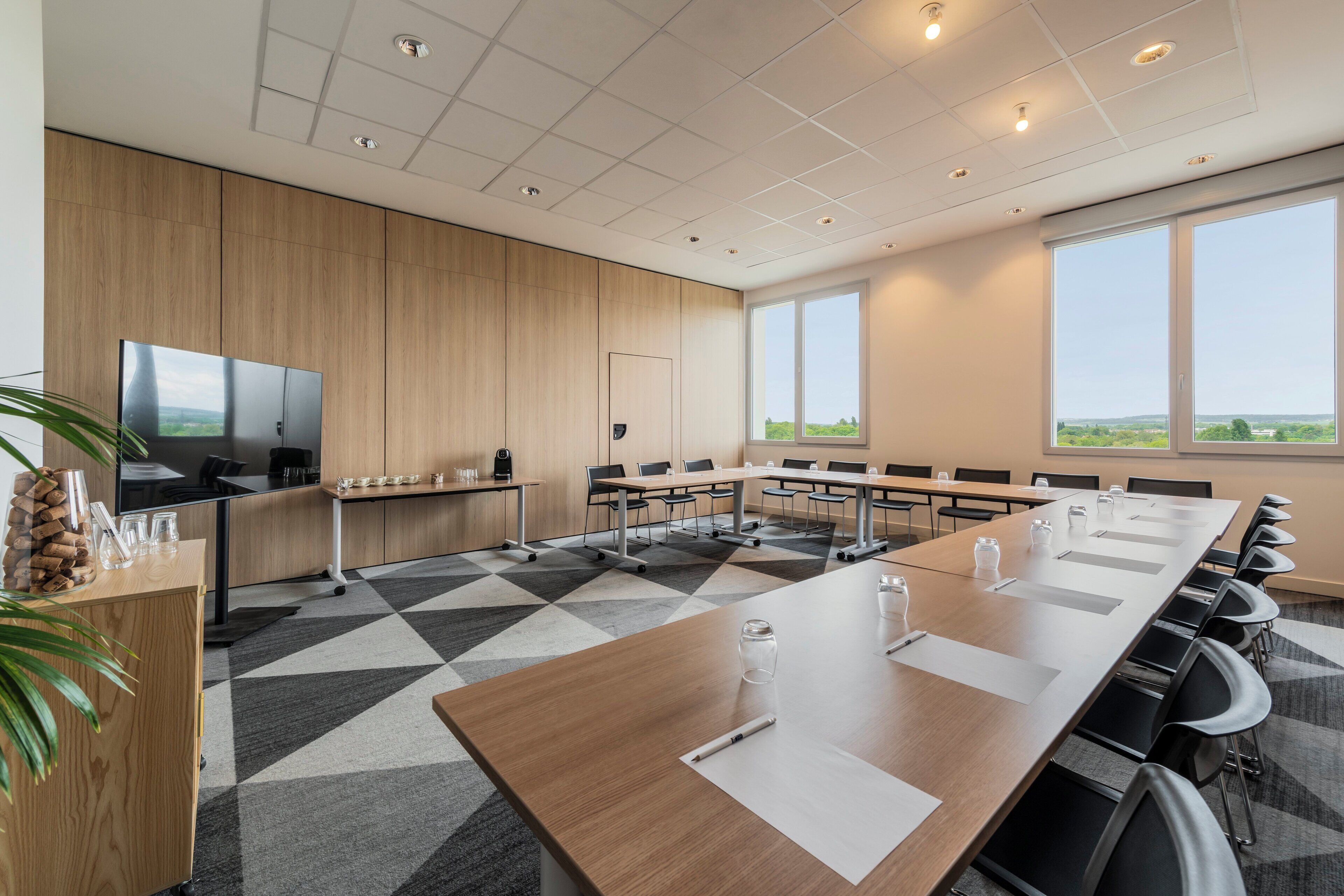 Une salle de conférence équipée d’une grande table, de chaises, d’un téléviseur et offrant une vue sur l’extérieur.