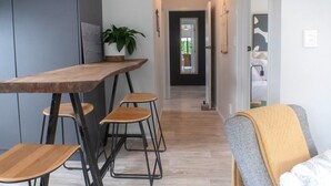 A modern kitchen with a wooden table and bar stools, a potted plant, and a hallway leading to a bedroom. - Quiet Escape with Lake Access and Kayaks | Peaceful Cosy Cottage (Rotorua)