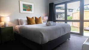 A hotel room with a large bed, two pillows, a framed picture on the wall, and a view of the outside. - Quiet Escape with Lake Access and Kayaks | Peaceful Cosy Cottage (Rotorua)