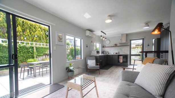 A modern living space with a sofa, a dining table, and a kitchen area. - Quiet Escape with Lake Access and Kayaks | Peaceful Cosy Cottage (Rotorua)